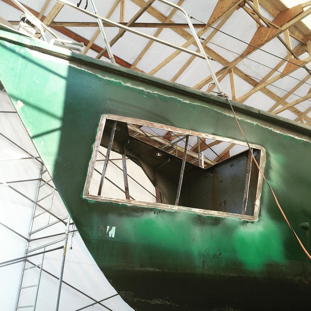 The hull of a green sailboat with a rectangular section cut out.