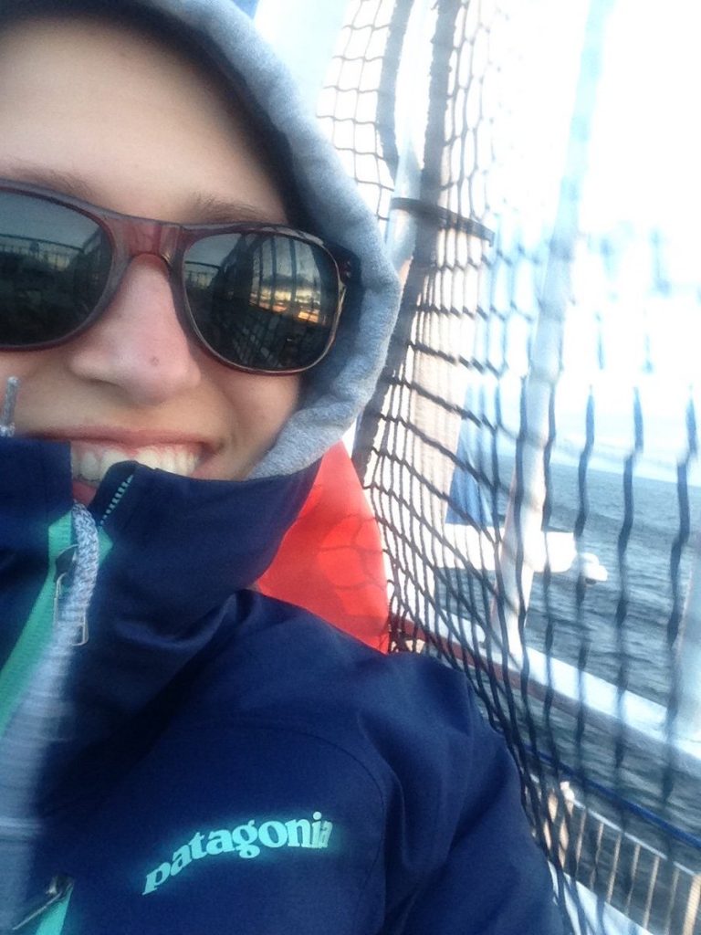 A blurry photo of a woman with hoodie and sunglasses smiling from behind her jacket.