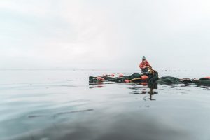A person in full rain gear crouches on a float of rope and buoy sitting on the water.