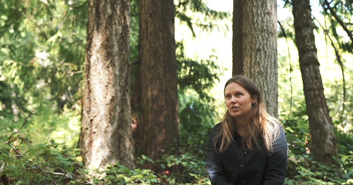 Megan Adams, biologist, sits in the forest to talk about her work in Wuikinuxv.