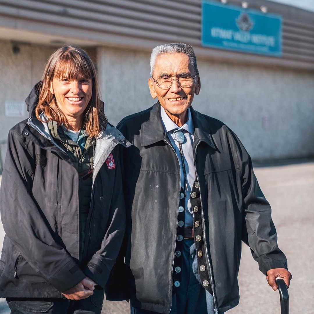 Two people stand close to each other smiling at the camera